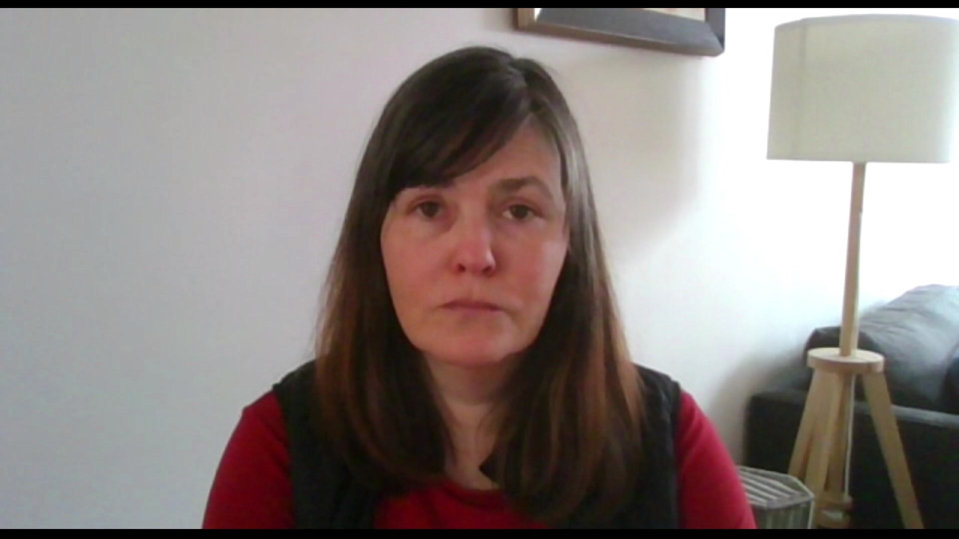 A woman in a red top looks at the camera.