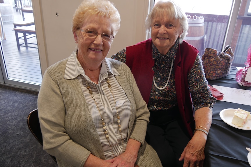 two older ladies sit side by side, grinning.