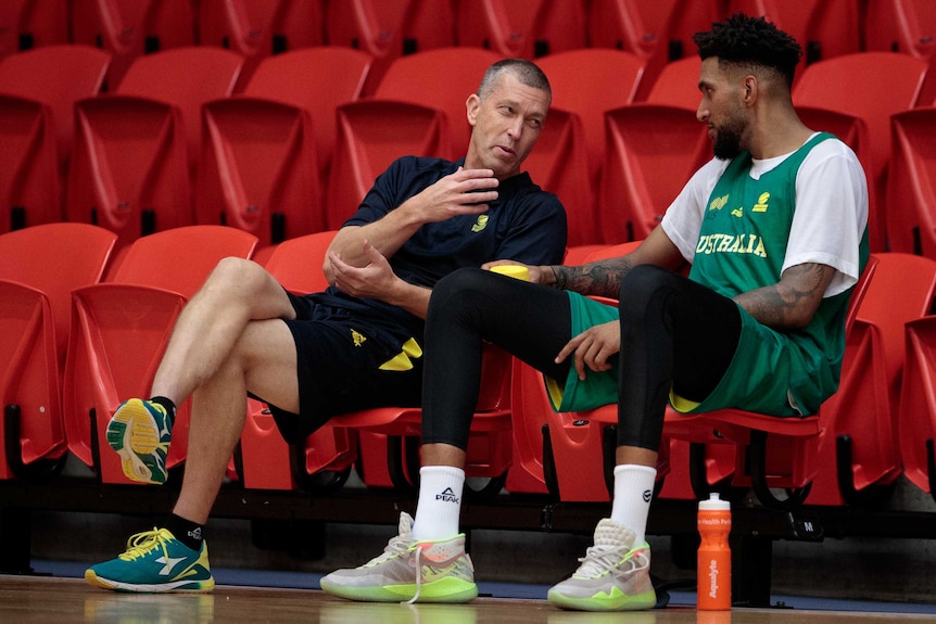 An Australian basketball coach sits with his legs crossed as he speaks to one of his players.