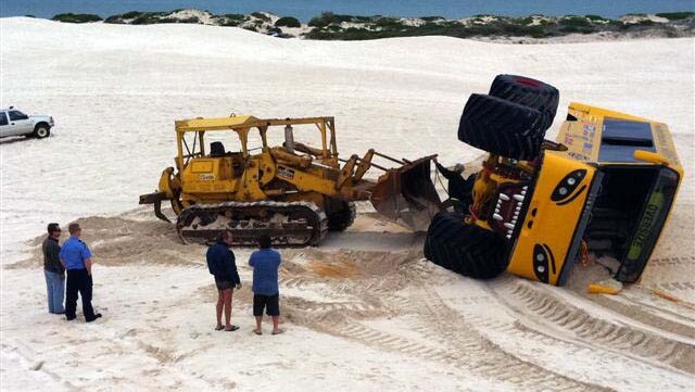 A front-end loader works to move a giant four-wheel-drive tourist bus on its side