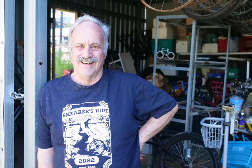 A man in a blue shirt standing in front of a shed full of trinkets 