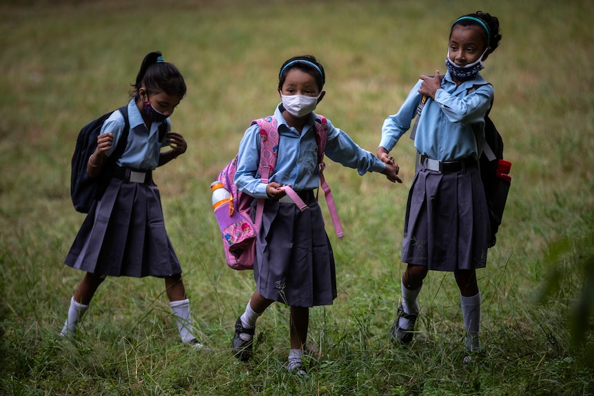 Three young girls stand in a field, wearing navy blue uniforms and face masks. 
