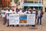 A group of people walk down a street. The people at the front hold a banner that reads 'water is life'. 