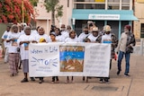 A group of people walk down a street. The people at the front hold a banner that reads 'water is life'. 