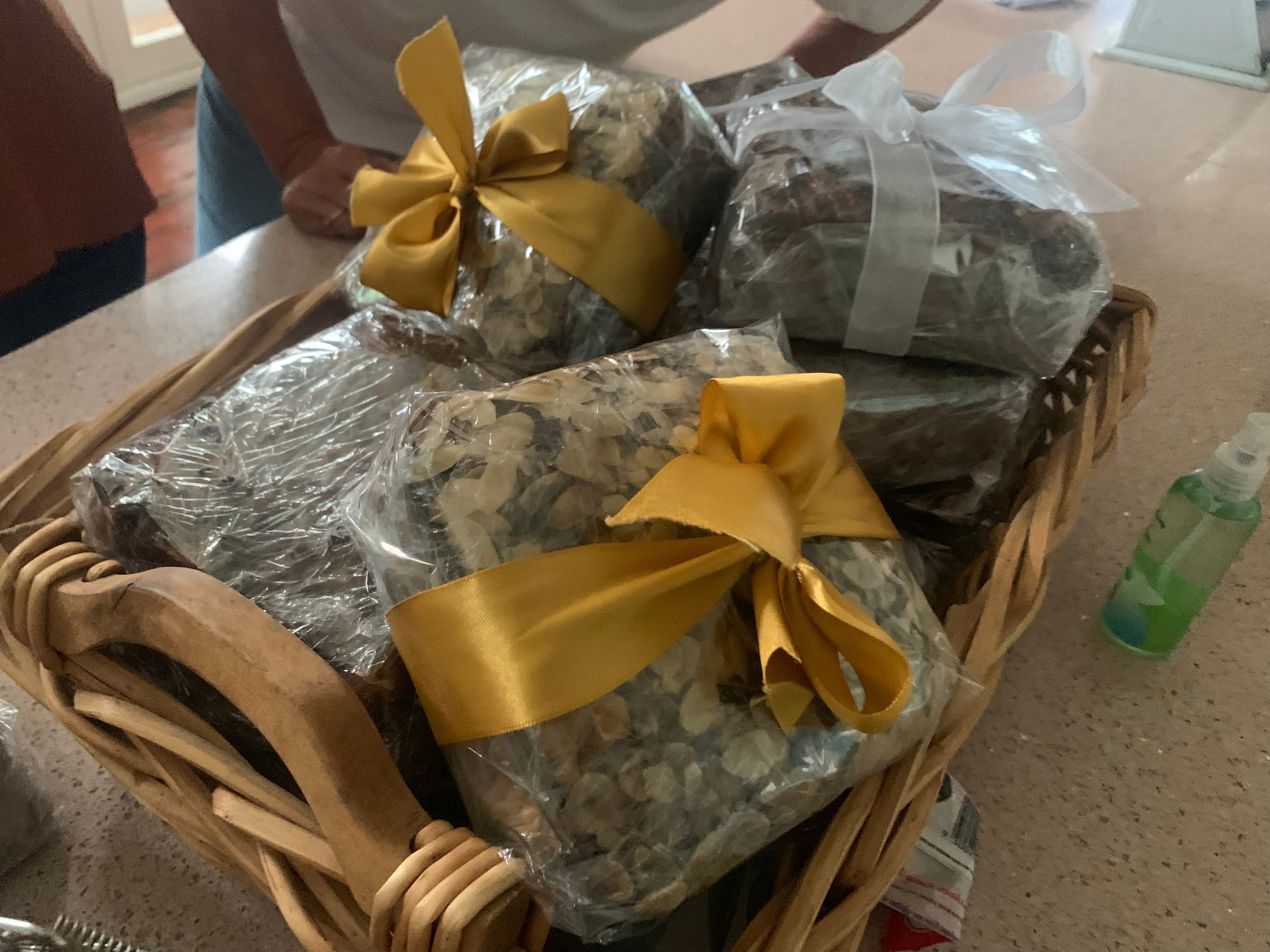 Uma coleção de bolos de Natal quadrados marrons está em uma cesta e com laços de ouro e prata.