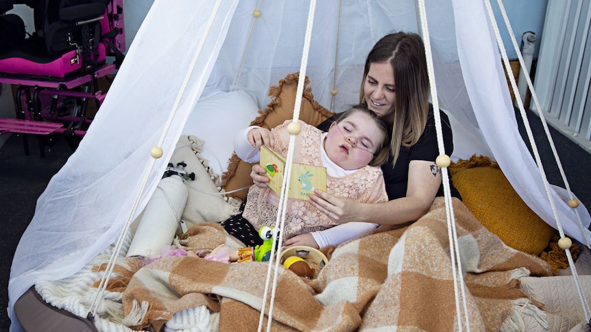 Mum and daughter snuggle up together in the play area, draped in netting and on pillows and blankets.