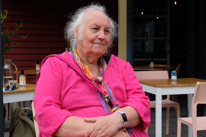 Toni sits with her arms crossed at a cafe.