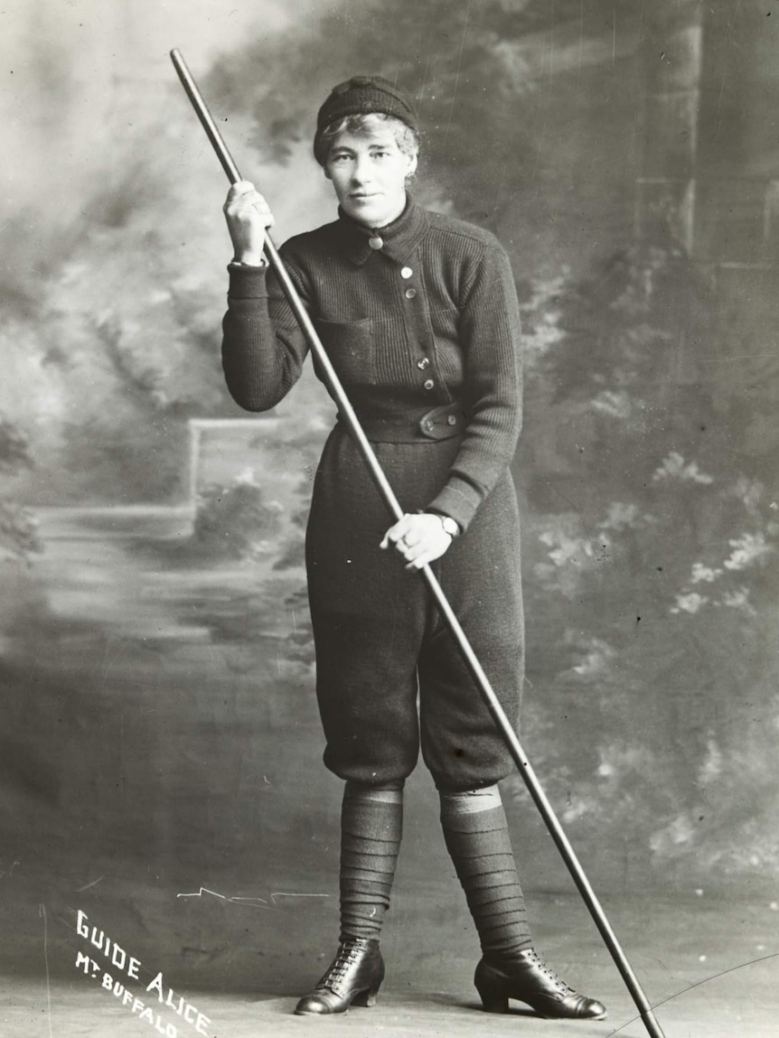 A woman with a large stick poses for the camera. Black and white.