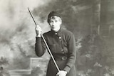 A woman with a large stick poses for the camera. Black and white.