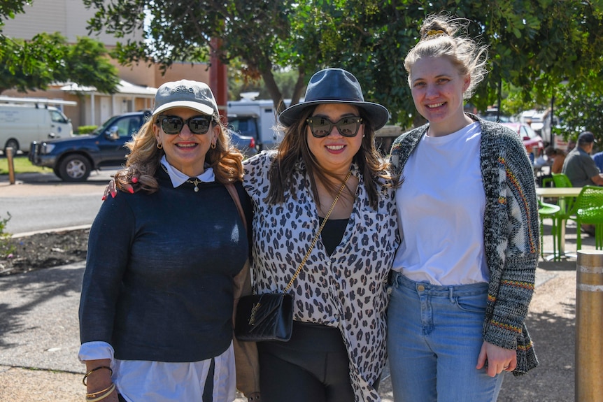 Three women on a busy street smile at the camera 