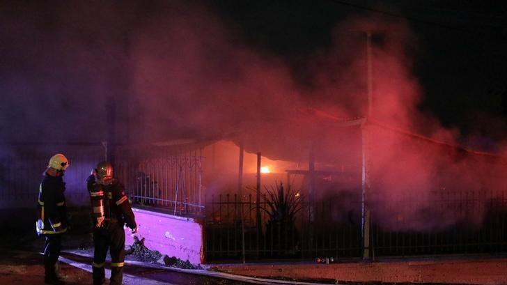 Firefighters stand next to a burning building at night outside the community centre on the island of Lesbos.