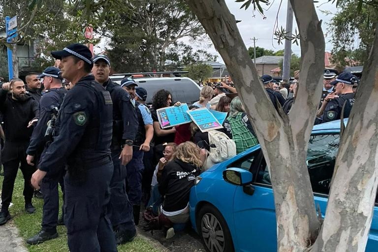 People cower between cars with placards held above their heads