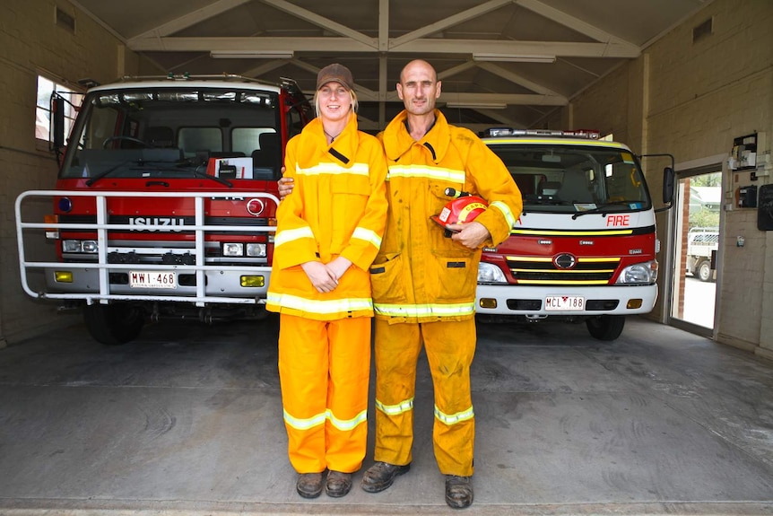 Man and young woman stand in yellow tunics in front of fire truck