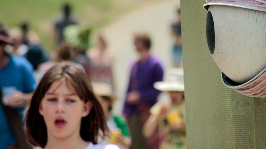 A girl walks past a wooden eyeball at the Woodford Folk Festival.