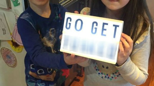 Two children wearing pyjamas hold up a lightbox with the words "go get f***ed" on it. The last word is blurred out.