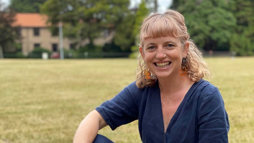 The writer Laura Jean McKay sitting on a grassy oval and smiling