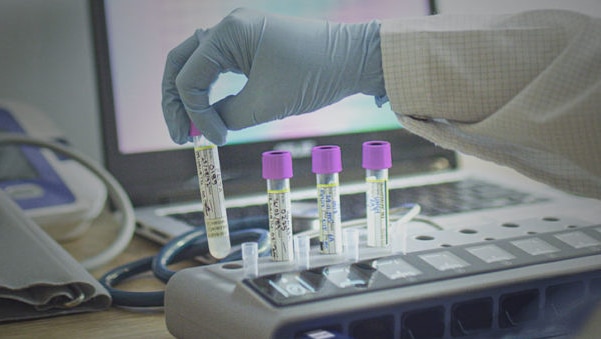 A gloved hand handles test tubes.