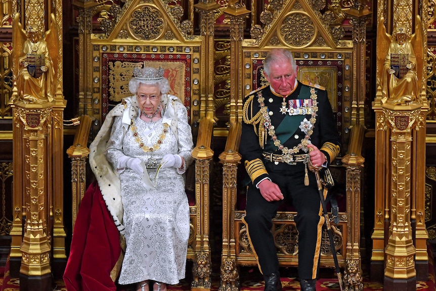 Queen and Prince Charles in full formal wear, on gold thrones