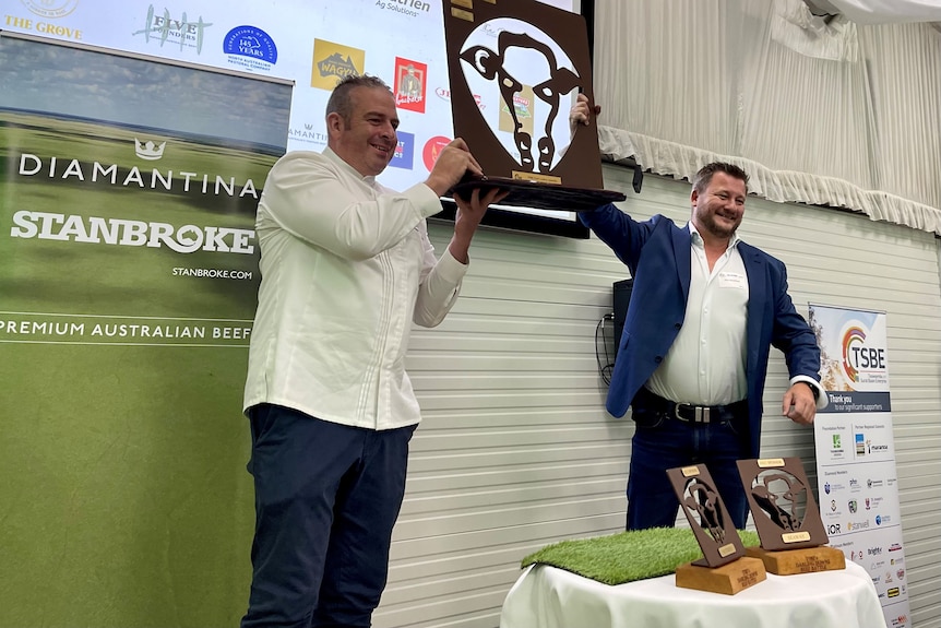 Two men holding up a trophy, which is shaped like a cow's head