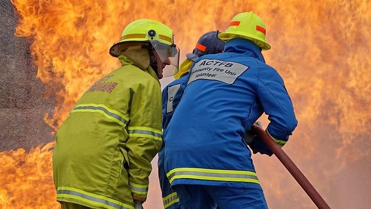 Three firefighters hose a large blaze as part of a training sesion