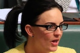 Emma Husar wears a pale yellow jacket with a blue shirt while sitting in question time, gesturing with both hands open.