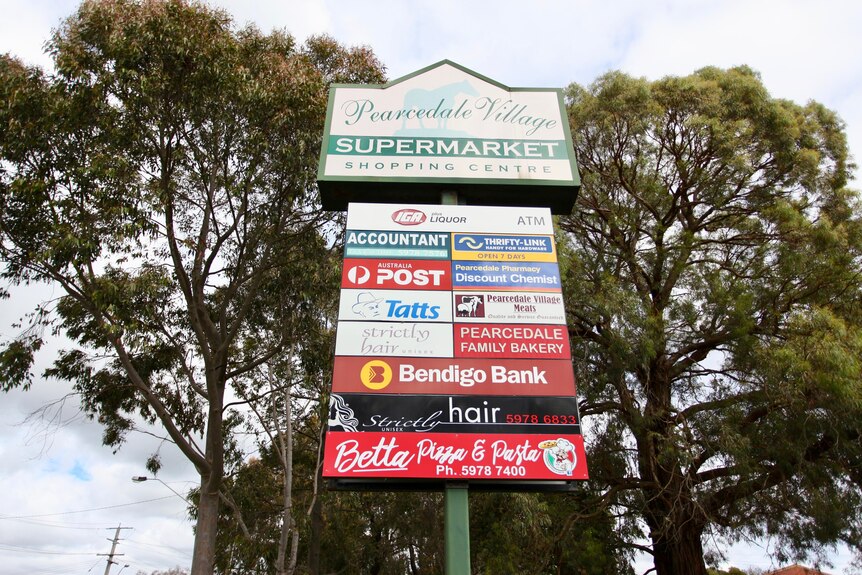 A sign in front of gum trees displays logos of IGA, post office, Bendigo Bank and other shops at Pearcedale Shopping Centre.