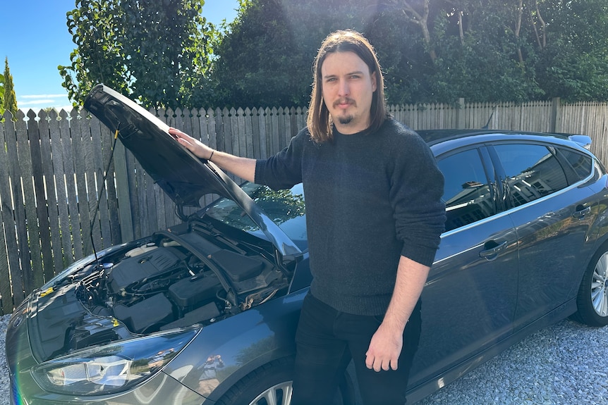 a man stands next to a car with the bonnet up