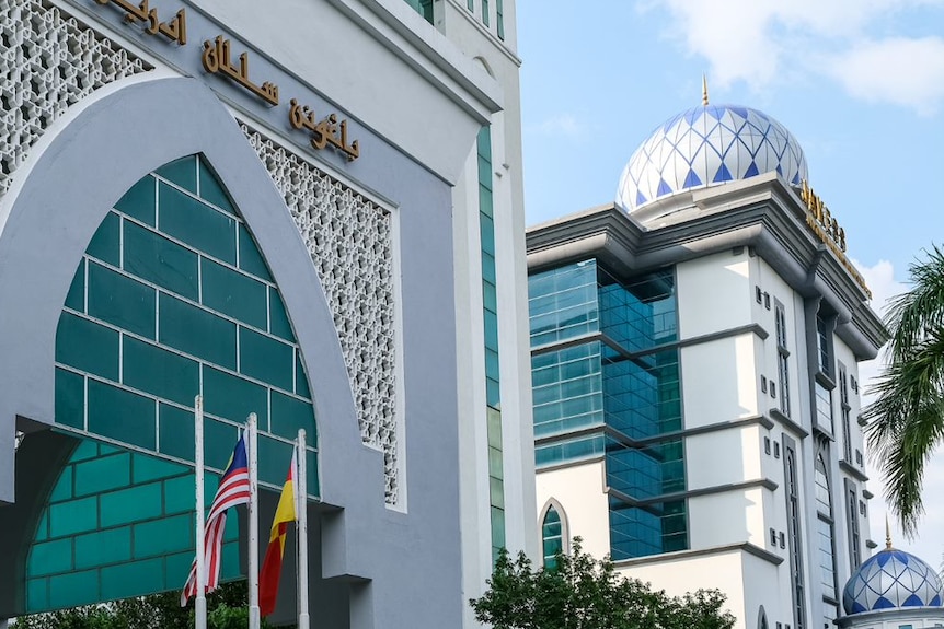 The front of a modern-looking Islamic building in Malaysia, with a mosque dome in the background.