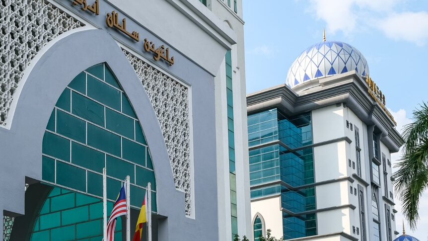 The front of a modern-looking Islamic building in Malaysia, with a mosque dome in the background.