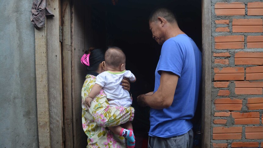 Mother holds baby with back to the camera while father stands in the doorway looking at them.