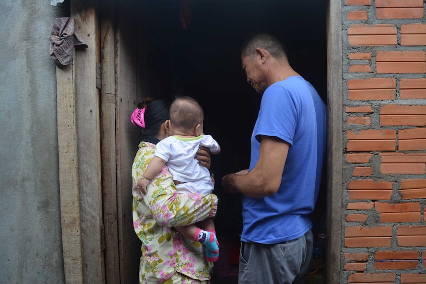 Mother holds baby with back to the camera while father stands in the doorway looking at them.