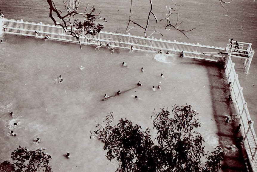 A black and white photo of people swimming in harbour baths.