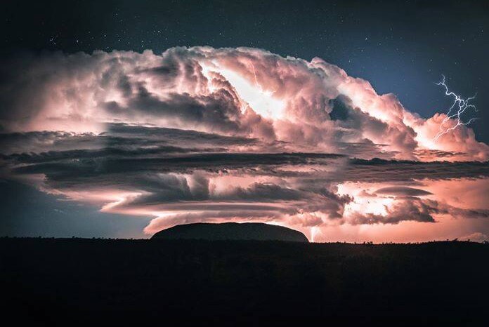 A large cloud hangs over Uluru, as lightning strikes close by