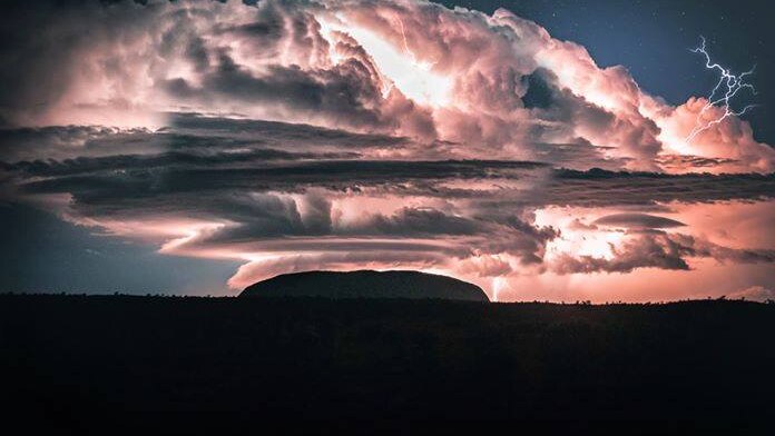 A large cloud hangs over Uluru, as lightning strikes close by