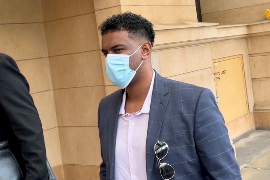 A man wearing a suit jacket and face mask outside a court building 