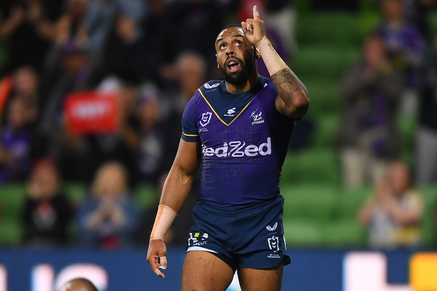 A Melbourne Storm NRL player looks up and points to the sky with a finger on his left hand.