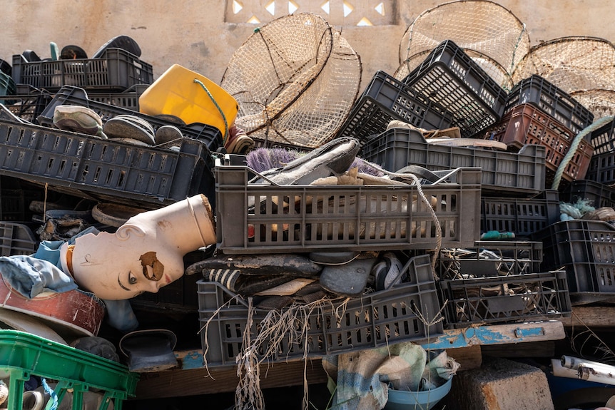 Plastic crates stuffed full of shoes are stacked on top of each other, with a mannequin head sticking out of one