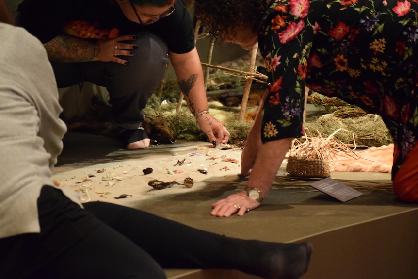 Three women sit with shells and seashore items in a museum.