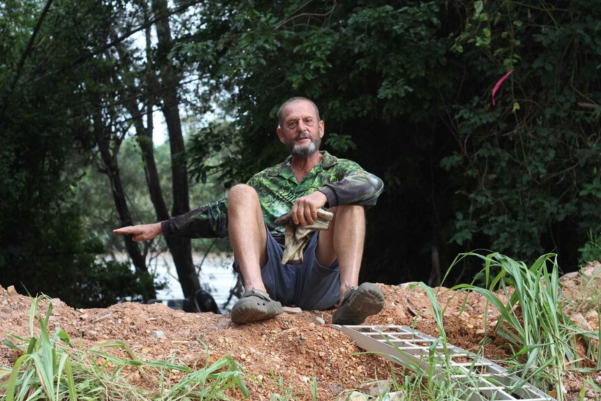 A man sitting on a sandbar gestures with his hand