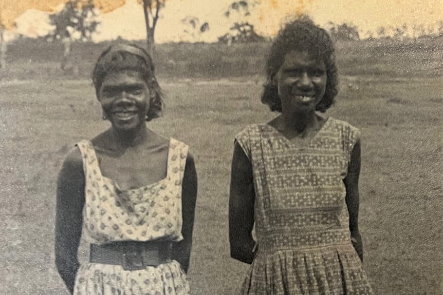 Two women stand side by side on a field. They are wearing sun dresses and are smiling.