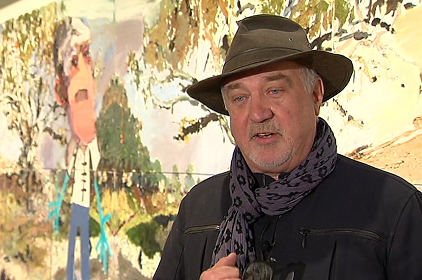 A man in a hat in front of a colourful artwork.