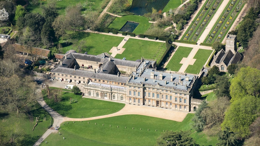 aerial view of large rectangular mansion, with other buildings and lush gardens and surrounds