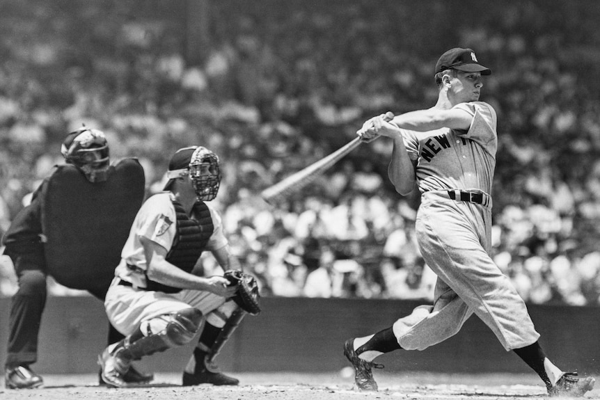 Mickey Mantle swings a baseball bat, standing in front of a catcher and umpire