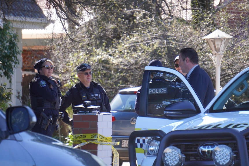 A man getting out of a police car with two police officers standing outside a house