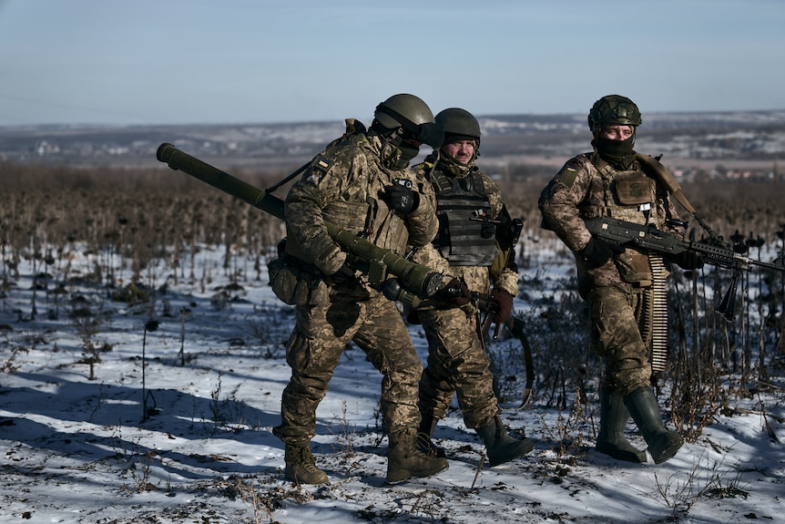Three Ukrainian soldiers carrying weapons through the snow.