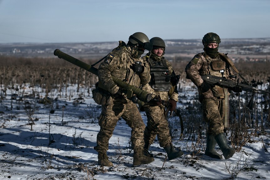 Three Ukrainian soldiers carrying weapons through the snow.