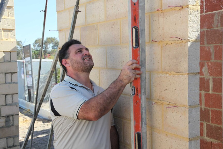 Man holding spirit level checks a wall on half built house