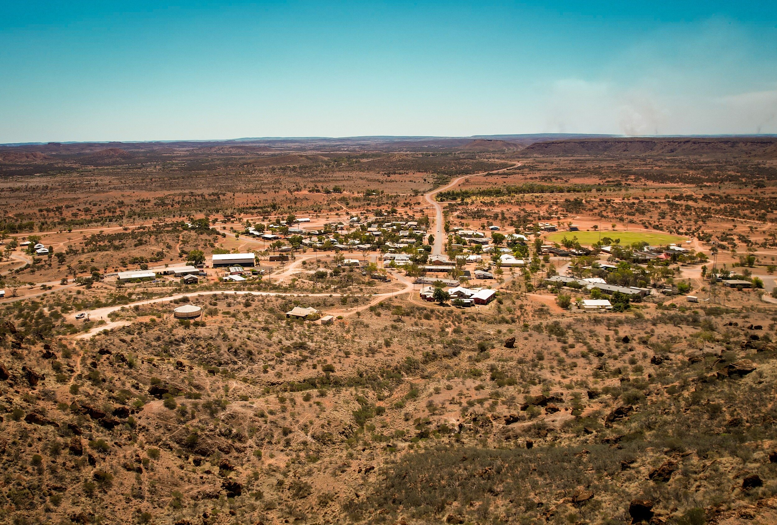 An aerial view of a small outback town, surrounded by scrub and red earth.