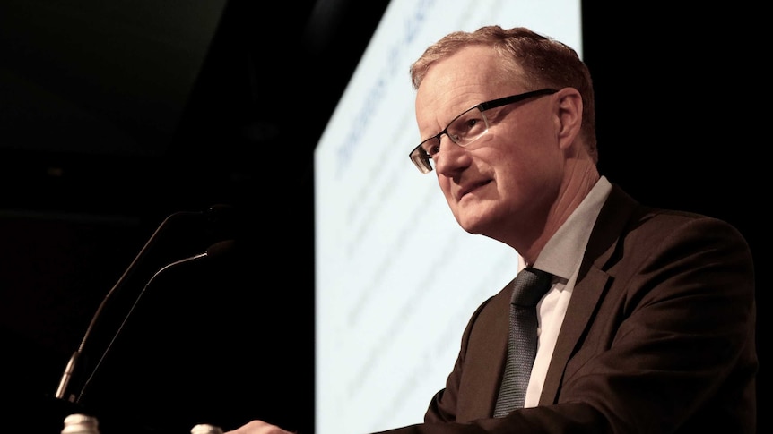 A man wearing a suit and glasses standing at a podium.