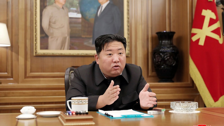 Kim Jong Un gestures with both hands while sitting at a desk